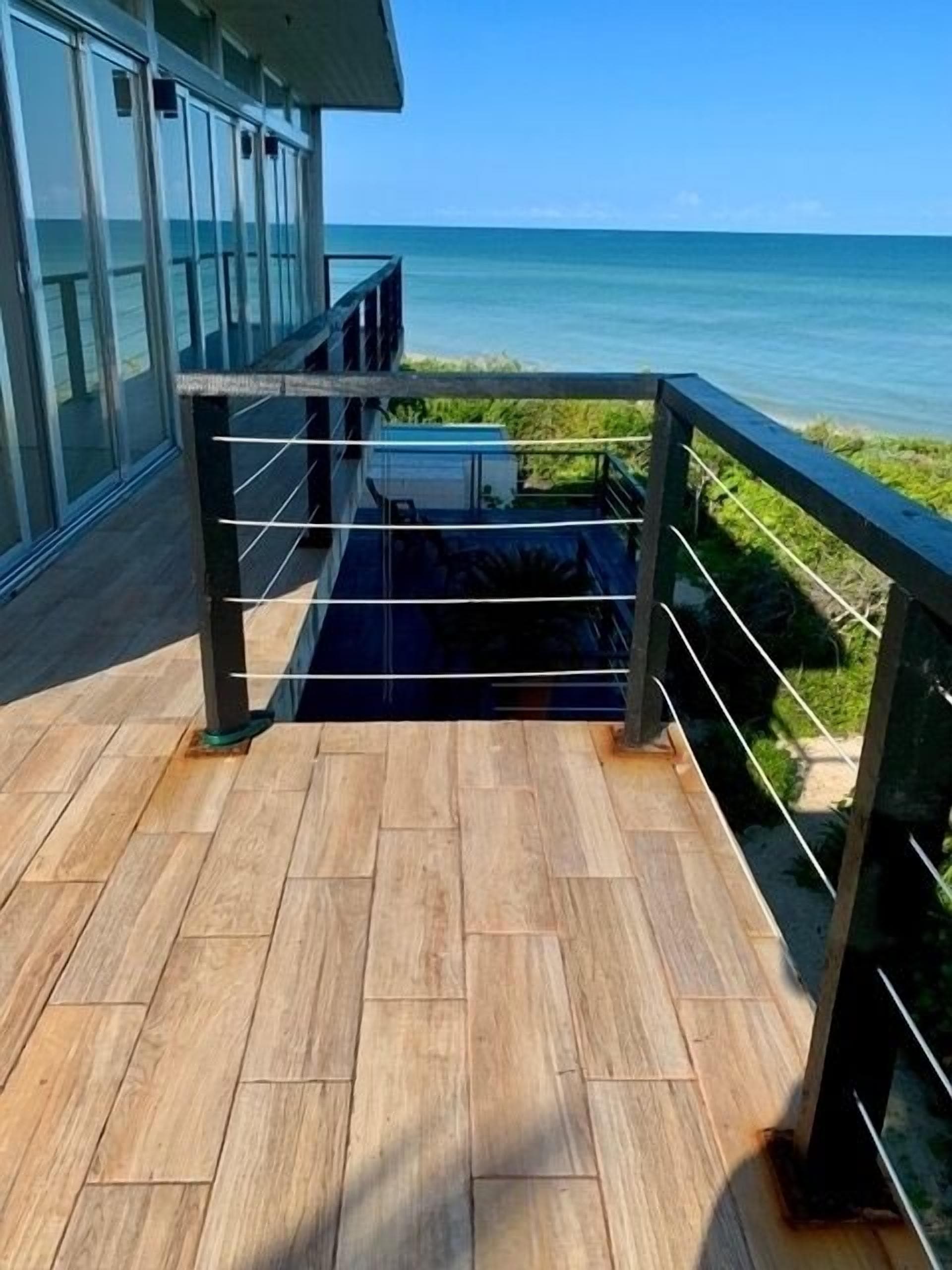 Une terrasse en bois dotée d’une balustrade en verre, qui offre une vue sur une étendue d’eau.