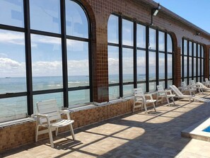 A poolside area with large windows overlooking the ocean, featuring sun loungers and a clear view of the sea.