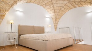 A bedroom with a large bed, two bedside tables, a radiator, and a white ceiling with a brick pattern.