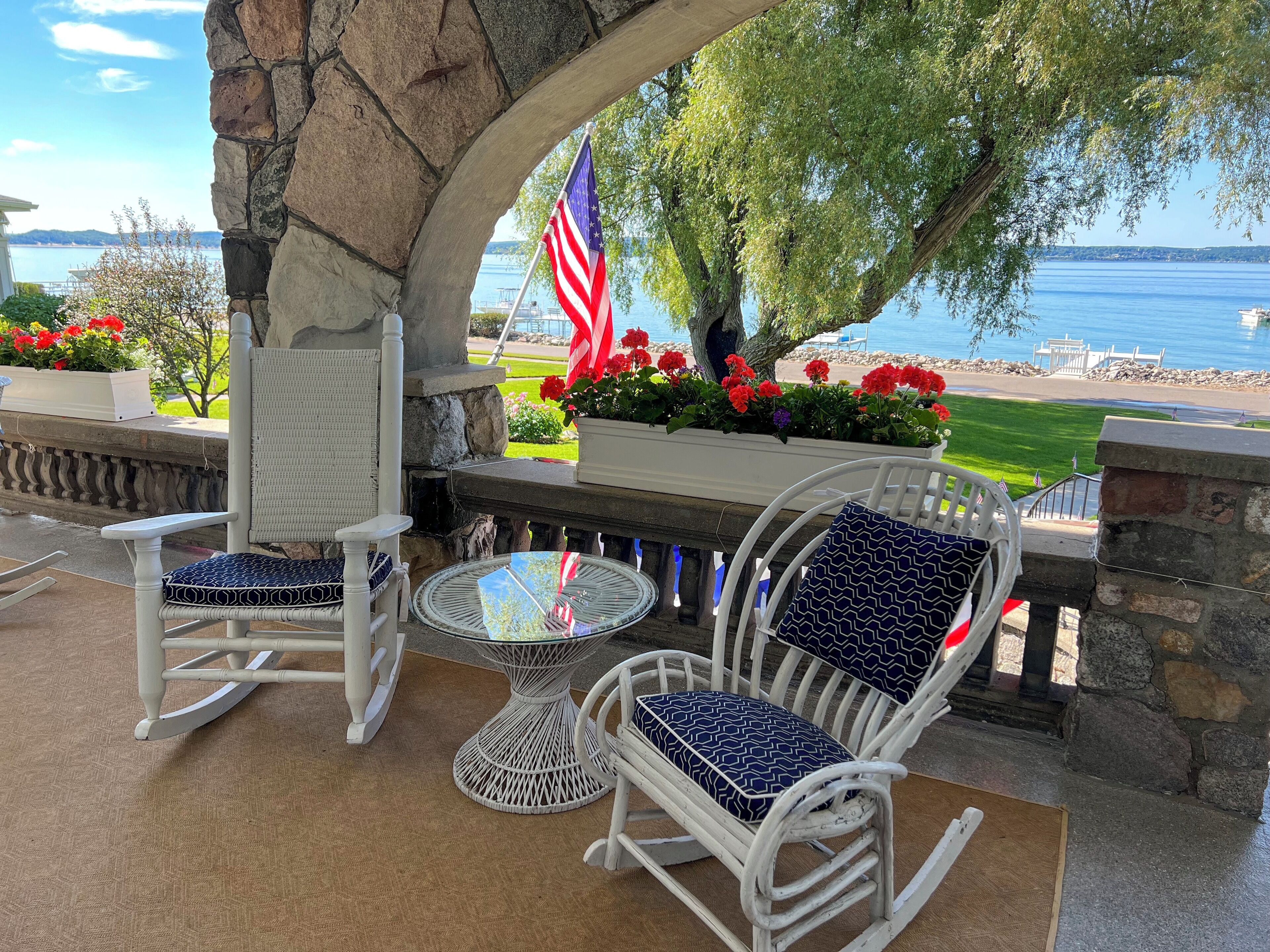 A patio area with white wicker furniture, a round table, and a view of the lake and beach.