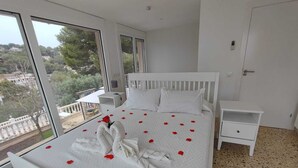 A bedroom with a large bed, two bedside tables, and a view of greenery outside.