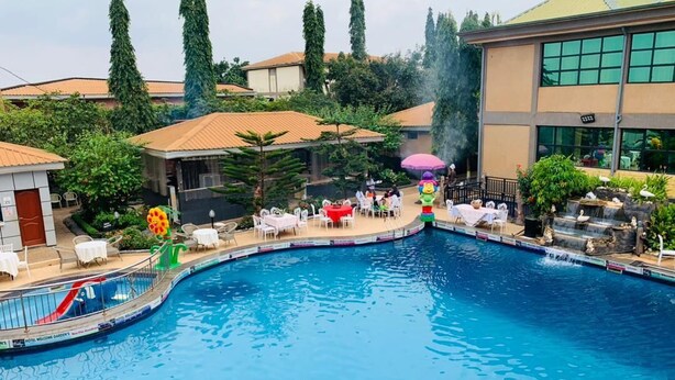 Una piscina con sillones de descanso y sombrillas, rodeada de vegetación y edificios.