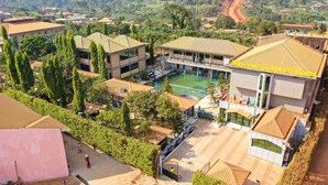 Un edificio de varios pisos con piscina, rodeado de vegetación y casas residenciales.