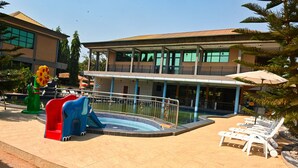 Un área de piscina con tobogán, sillas de descanso y un edificio con amplias ventanas y balcones.