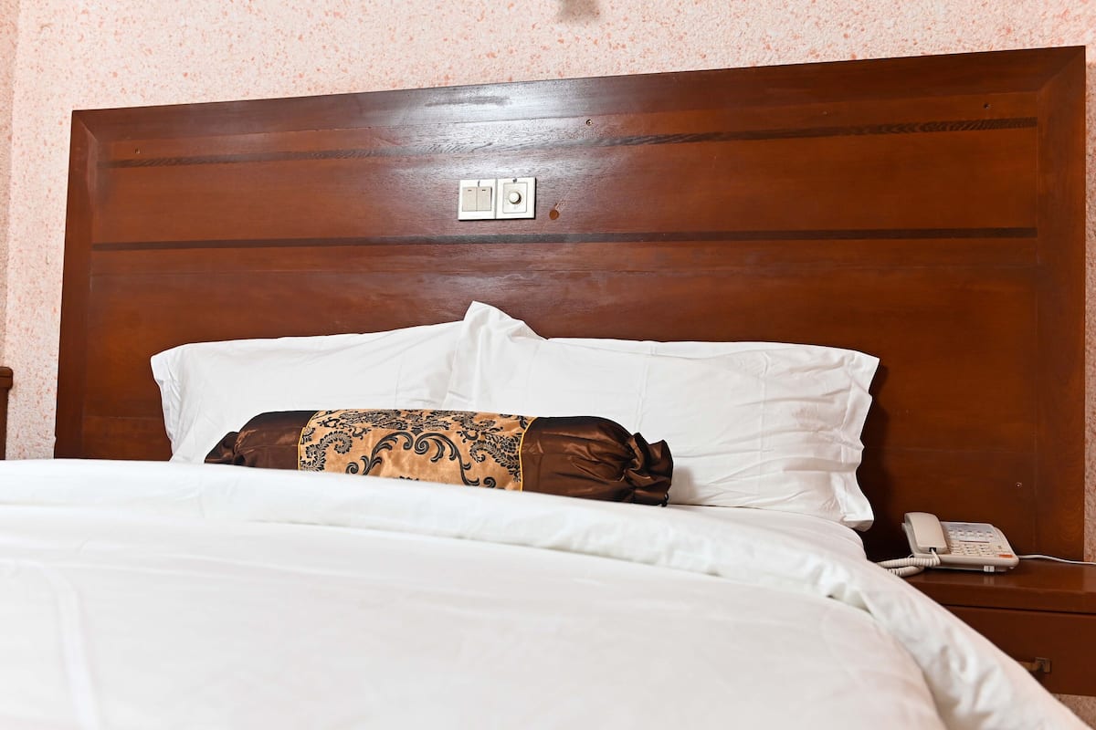 A neatly made bed with white linens, a brown patterned pillow, and a bedside telephone on a wooden nightstand.