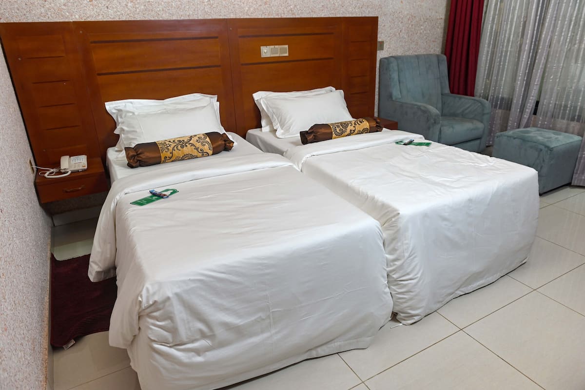 A hotel room with two beds, a wooden headboard, a blue armchair, and a small table.