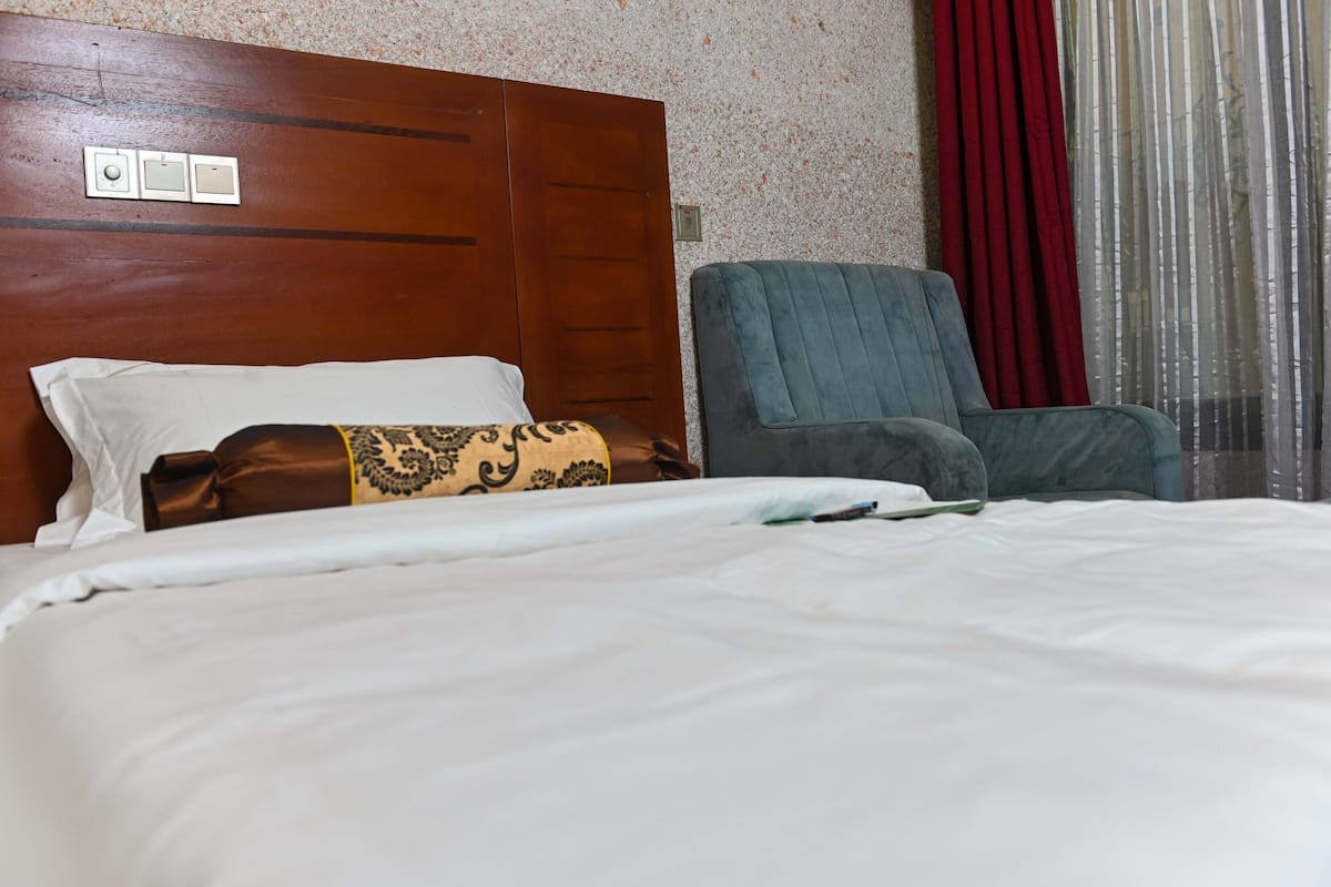 A hotel room with a bed, a chair, a wooden headboard, and a wall with a textured pattern.
