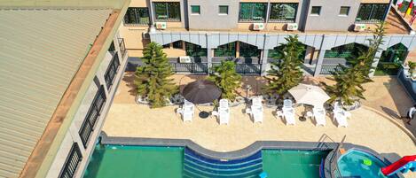 An aerial view of a hotel with a swimming pool, sun loungers, and a children's play area.