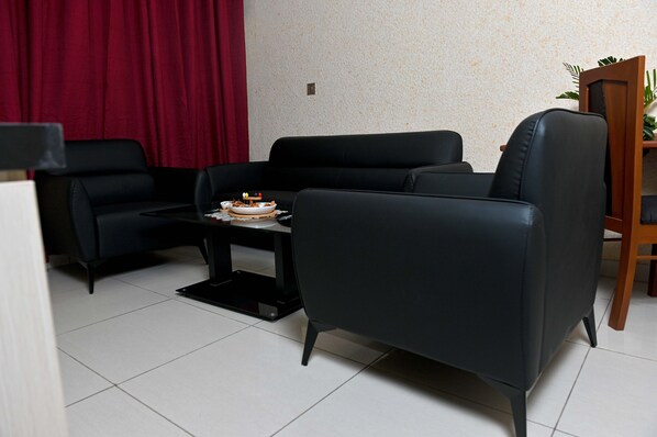 Un salon avec un canapé noir, une petite table sur laquelle se trouve un gâteau et un rideau rouge.