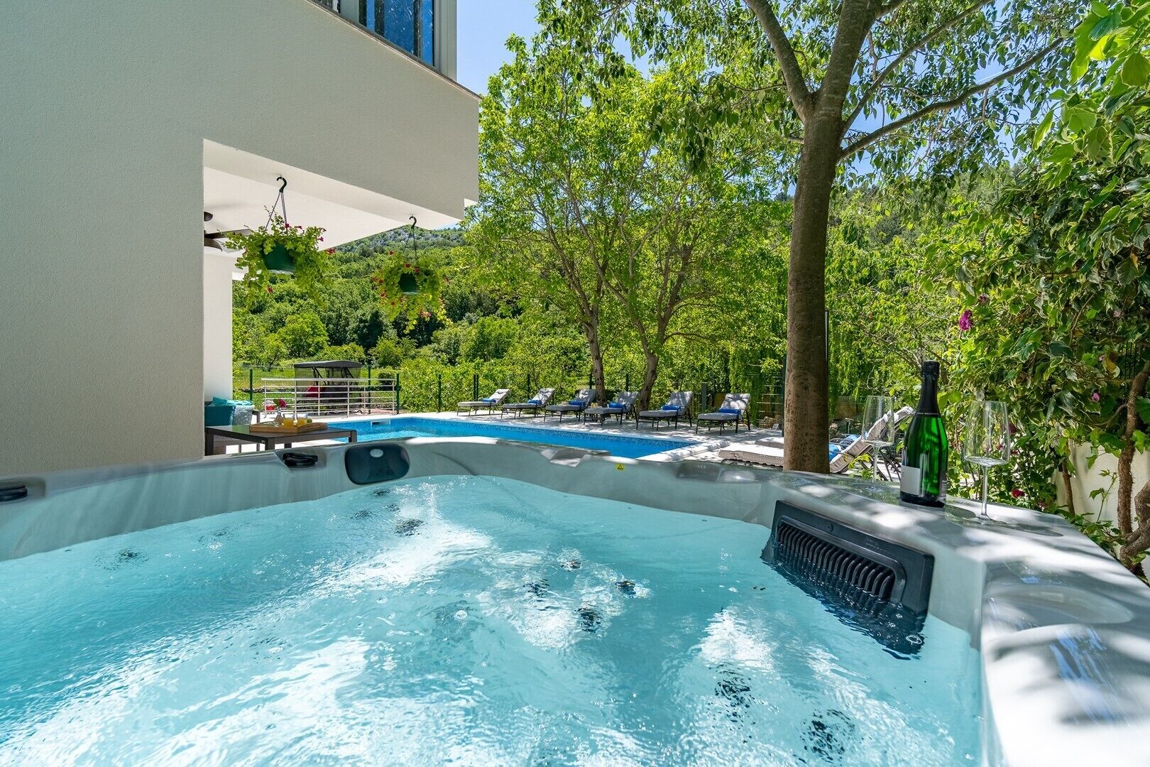 Et område med jacuzzi, swimmingpool, liggestole og en flaske vin.