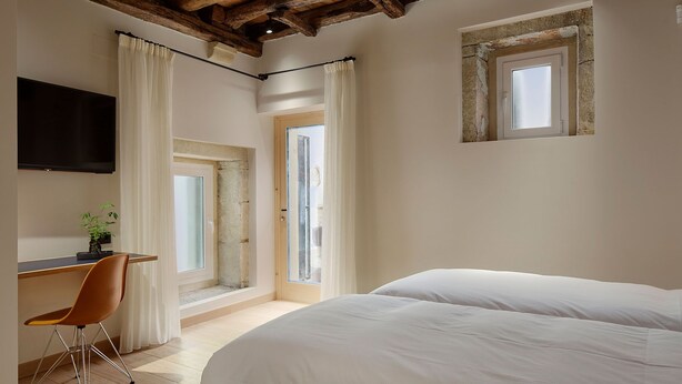 Un dormitorio con cama, escritorio y silla, televisor y ventana con cortinas.