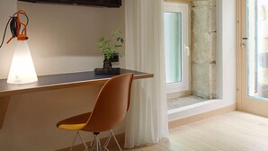Una habitación moderna con techo de madera, un televisor de pantalla plana montado en la pared, un escritorio con lámpara, una silla y una ventana con cortinas.