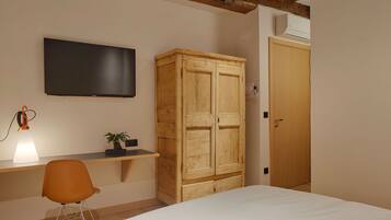 A bedroom with a bed, a desk with a chair, a television, a wardrobe, and a bedside lamp.