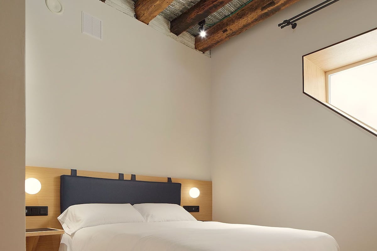A bedroom with a wooden floor, a bed with white bedding, a wooden headboard, and two bedside lamps.