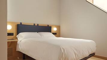 Un dormitorio con suelo de madera, cama con ropa blanca, cabecero de madera y dos lámparas de noche.