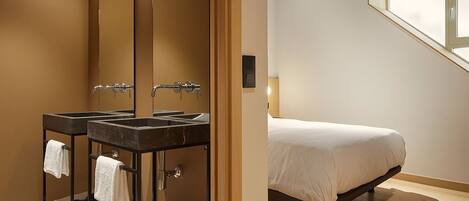 A modern bathroom with two sinks, a large mirror, and a bed with a window above it.