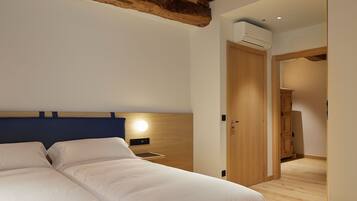 Un dormitorio con una cama grande, cabecera de madera, una mesita de noche con lámpara y una puerta que da a otra habitación.