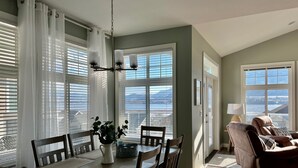 A dining area with a table set for four, a chandelier, and a view of a lake and mountains through large windows. - Beach, boatslip, 2 pools, 2 hottubs, 4 bdrm house sleeps 12 (Oliver)