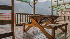 Una terraza de madera con una mesa de picnic, barandillas de metal y vistas a montañas.
