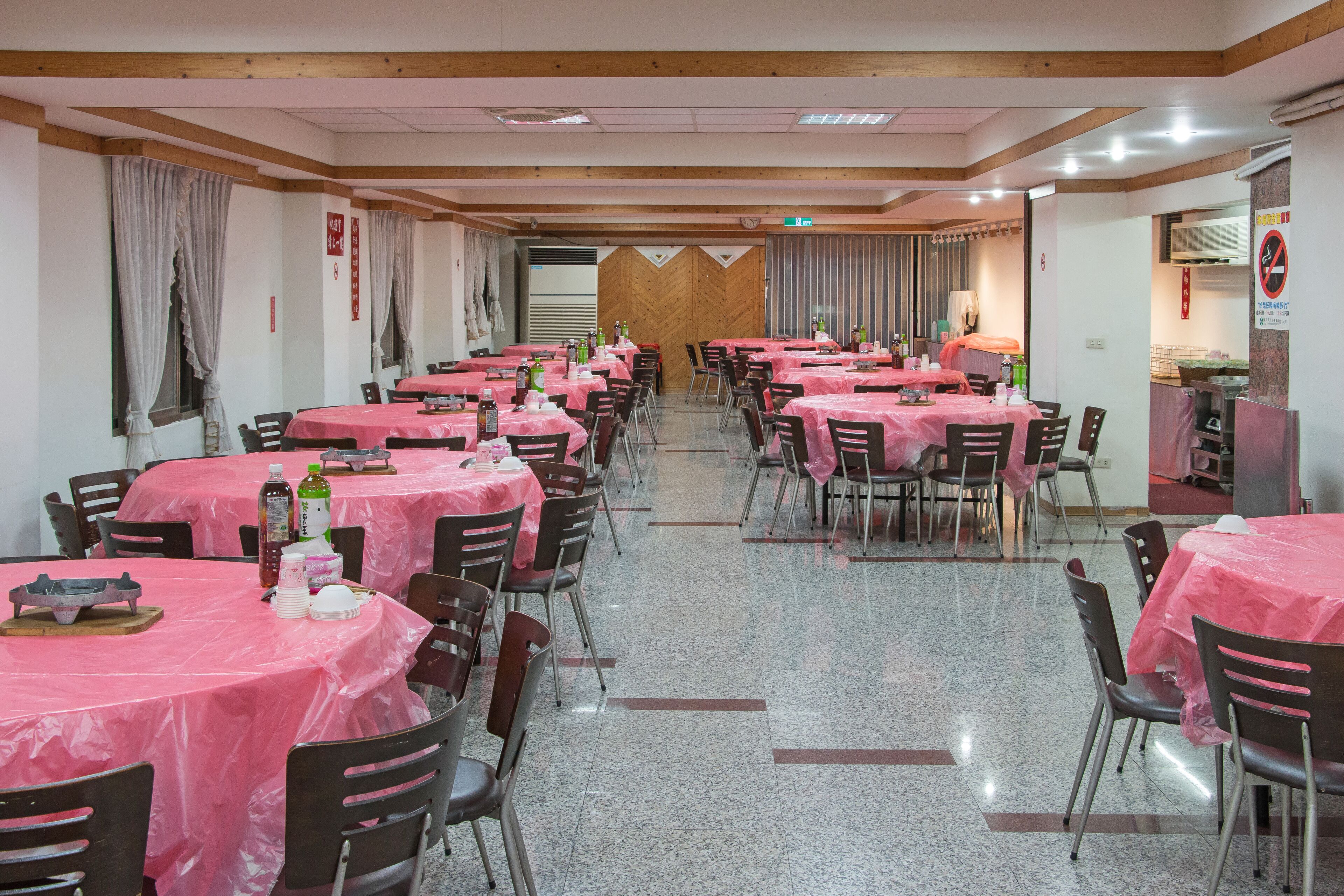A dining area with multiple tables covered in pink tablecloths, arranged in rows.