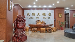 Un área de recepción con una estatua de madera, una gran mesa de madera y un letrero que dice "TONG PU HOTEL".