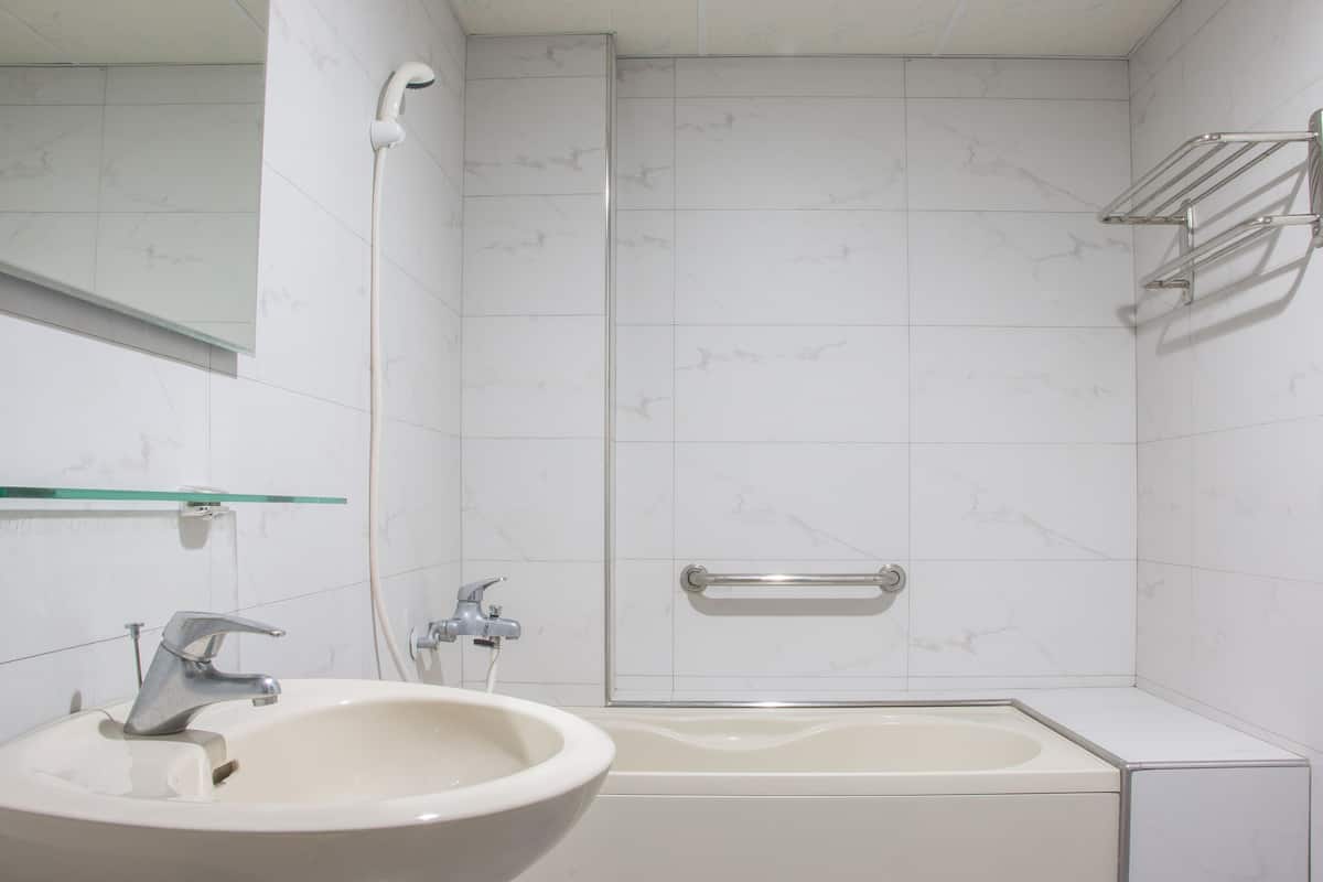 A bathroom with a sink, mirror, shower, and towel rack.