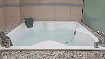 A bathtub with a glass door, a shower head, and a control knob.