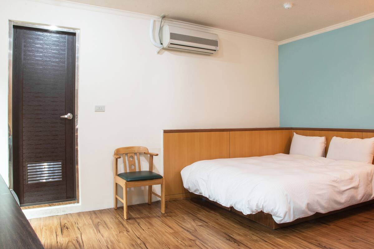 A bedroom with a wooden bed, a chair, a door, and an air conditioning unit.