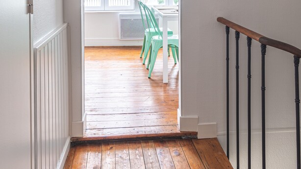 Een houten vloer die leidt naar een balkon met een witte reling, een hangende lamp en uitzicht op een terras met stoelen.