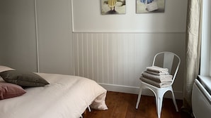 Een slaapkamer met een bed, een stoel met handdoeken en twee schilderijen aan de muur.