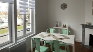 Een eethoek met een witte tafel, groene stoelen, een klein bijzettafeltje met decoratieve objecten en een open haard.