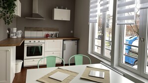 Een moderne keuken met witte kasten, een ingebouwde oven en een vaatwasser. Er staan twee groene stoelen en een witte tafel met placemats.
