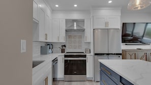 A modern kitchen with white cabinetry, stainless steel appliances, and a marble countertop.