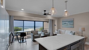 Una habitación de hotel moderna con una cocina central grande, una zona de estar con vista al océano y un ventilador de techo.