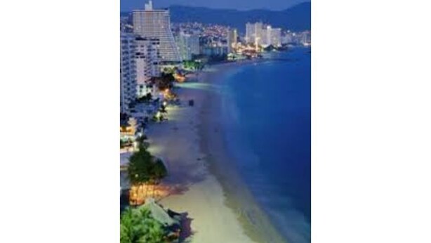 A coastal cityscape at night with high-rise buildings, a beach, and a clear sky.