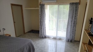 A bedroom with a bed, a desk, a TV, and a window with curtains.