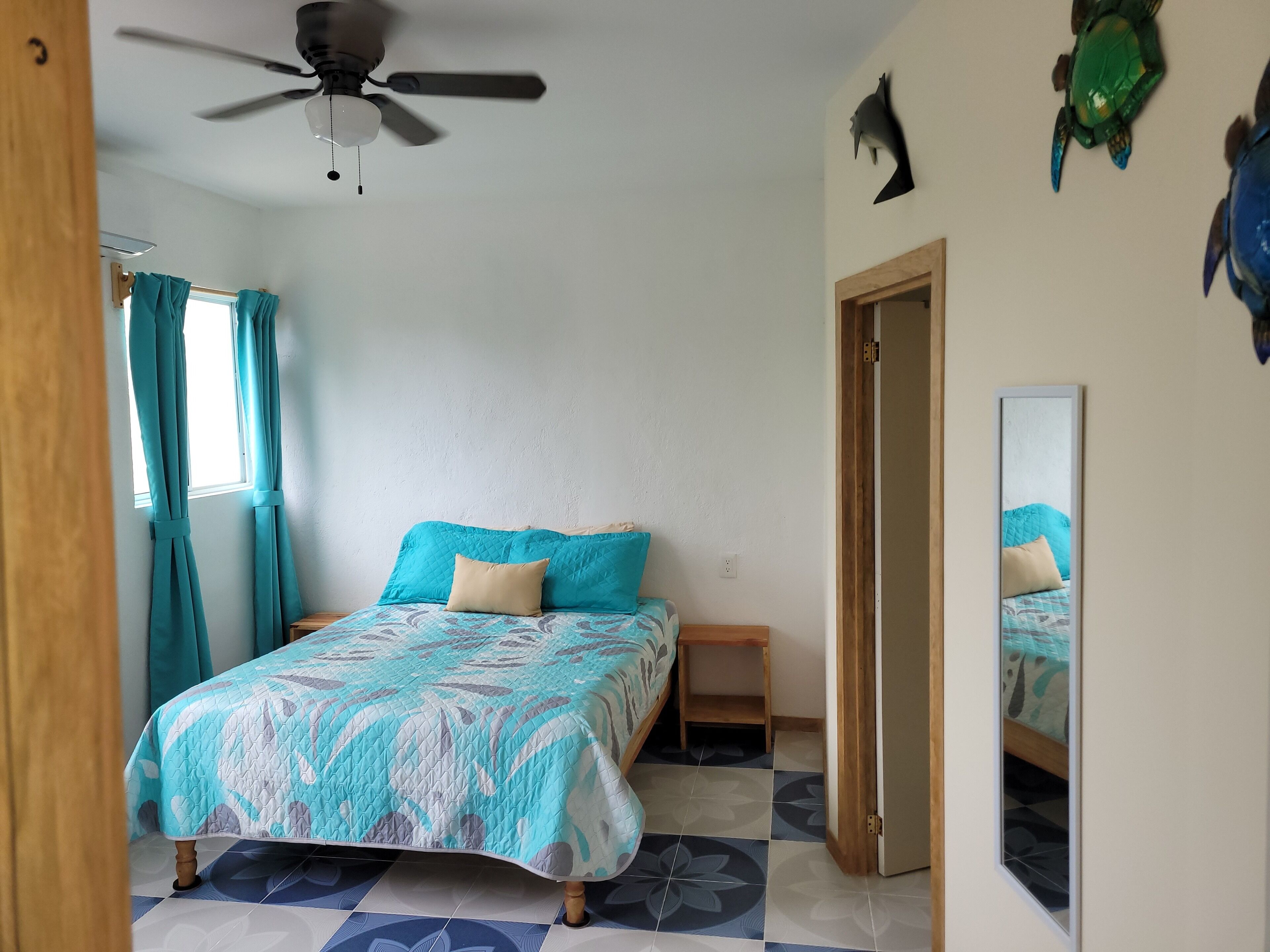 Une chambre à coucher avec un lit, un ventilateur de plafond, une fenêtre avec des rideaux et un miroir.