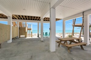 Un espacio al aire libre techado, con piso de concreto, mesa de picnic de madera y sillas de playa.