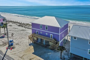 Una casa de playa de dos pisos con un balcón, una escalera y vista al océano.