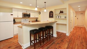A modern kitchen with white cabinets, a central island with bar stools, a microwave, and a clock on the wall. - Beach View, Next to Pool, 2nd floor- Club at Mexico Beach 2J (Mexico Beach)