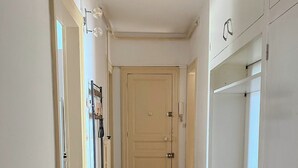 Un couloir doté d’un plancher en bois, une porte et une petite table sur laquelle se trouve une bougie.