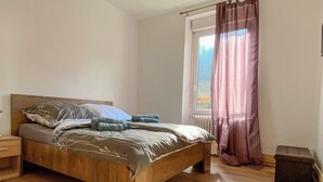 Une chambre à coucher avec un lit en bois, une table de chevet, une fenêtre avec des rideaux et un radiateur.