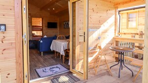 A wooden cabin interior with a dining area, a sofa, and a small table. - Clover Lodge (Leiston)