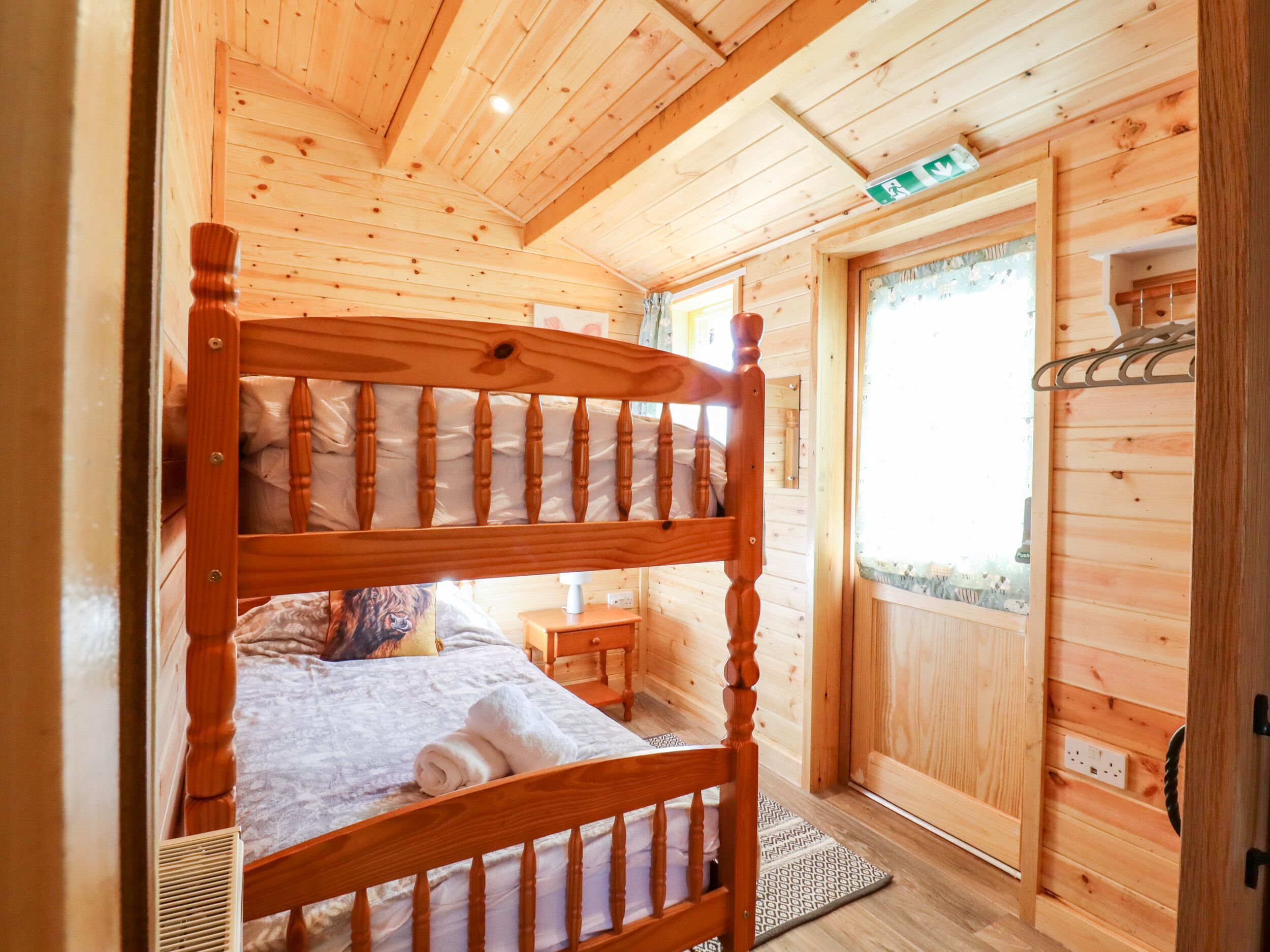 A wooden cabin room with a bunk bed, a small bedside table, and a window with a view.
