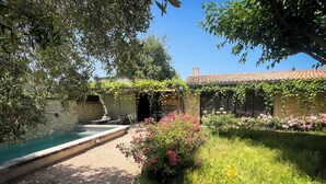 Et privat poolområde med en stenvæg, en pergola og en have med lyserøde blomster.