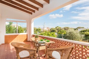 A balcony with wicker furniture, a table, and a view of greenery and buildings. - 3 bedroom villa in Punta Prima - Paula (Punta Prima)