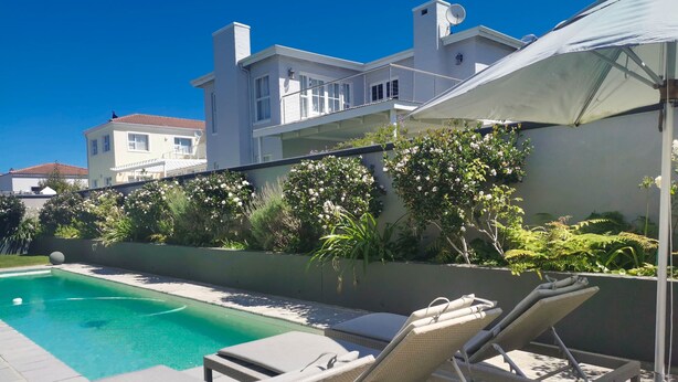 A swimming pool with lounge chairs, surrounded by a garden with various plants and flowers. - Vitamin Sea (Plettenberg Bay)