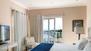 A hotel room with a bed, a desk with a TV, a chair, a balcony with a view, and a lamp. - Vitamin Sea (Plettenberg Bay)