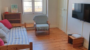 A bedroom with a bed, a chair, a TV, and a window with a view of buildings. - Beautiful renovated apartment, 5 min from the beach! (BIARRITZ)