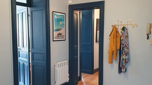 A hallway with wooden flooring, a geometric ceiling light, and a coat rack with jackets. - Beautiful renovated apartment, 5 min from the beach! (BIARRITZ)